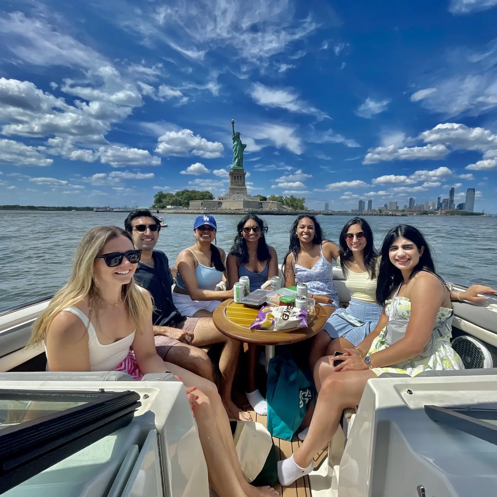 A group enjoying charter drinks and snacks with the Statue of Liberty and NYC skyline behind them