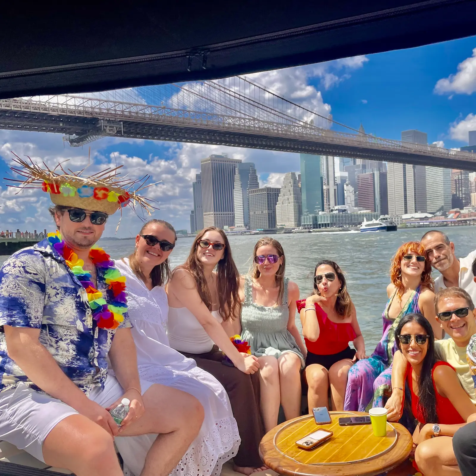 Guests celebrating on a New York Charters trip under the Brooklyn Bridge with the Manhattan skyline behind them